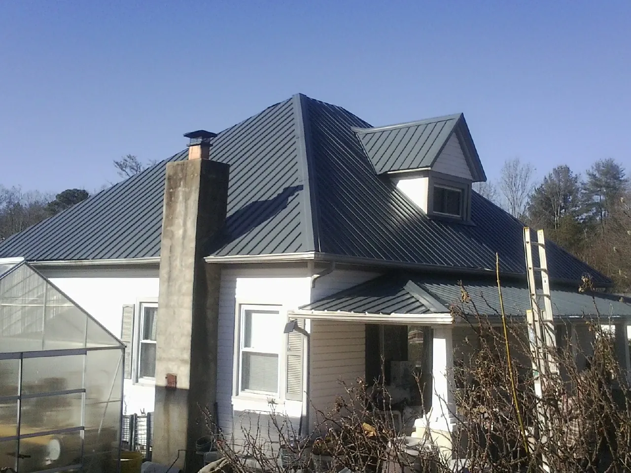 Dark blue standing seam metal roof on a white farmhouse with dormer — Slate & Tile Roof Repair by Roofing Brothers in Williamston