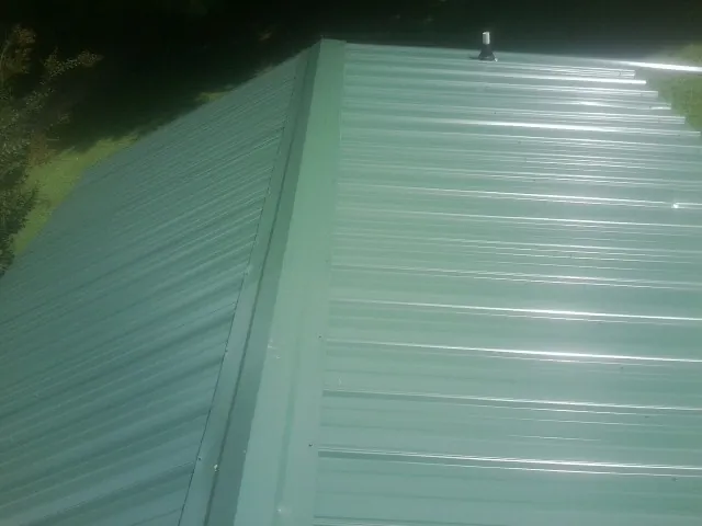 New green metal panels meeting at the ridge of a roof — Flat Roof Repair work by our crew in Williamston