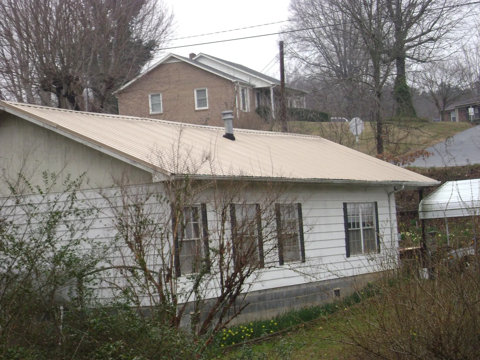 Tan metal roof on a white sided house set into a hillside — Commercial Roofing by Roofing Brothers in Williamston
